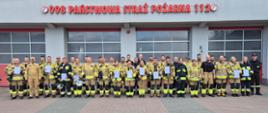 Uczestnicy szkolenia podstawowego strażaka ratownika OSP po zakończeniu kursu, ustawieni do wspólnego zdjęcia przed budynkiem Komendy Powiatowej PSP w Przasnyszu.