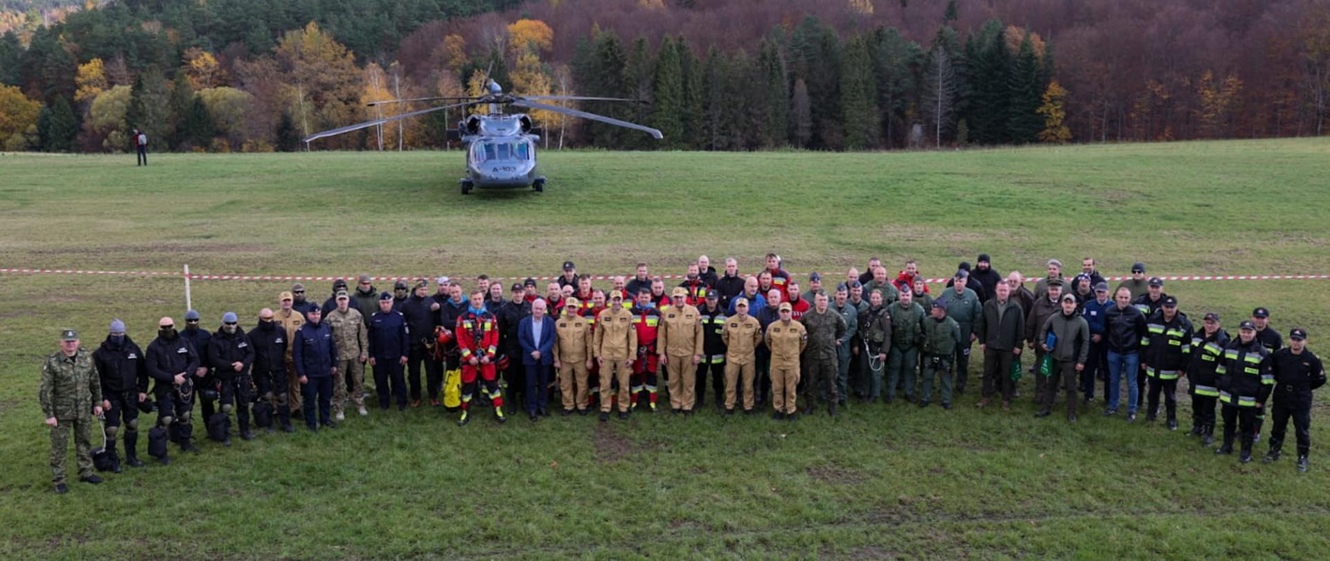 Zdjęcie grupowe wszystkich uczestników manewrów na murawie lotniska. W tle śmigłowiec i zalesione pagórki. 