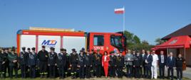 Wspólne zdjęcie druhów Ochotniczej Straży Pożarnej w mundurach wyjściowych oraz w koszarowych, ,Kujawsko-Pomorski Komendant Wojewódzki Państwowej Straży Pożarnej nadbrygadier Jacek Kaczmarek a także przedstawiciele samorządowi, w tle samochód ratowniczo-gaśniczy.
