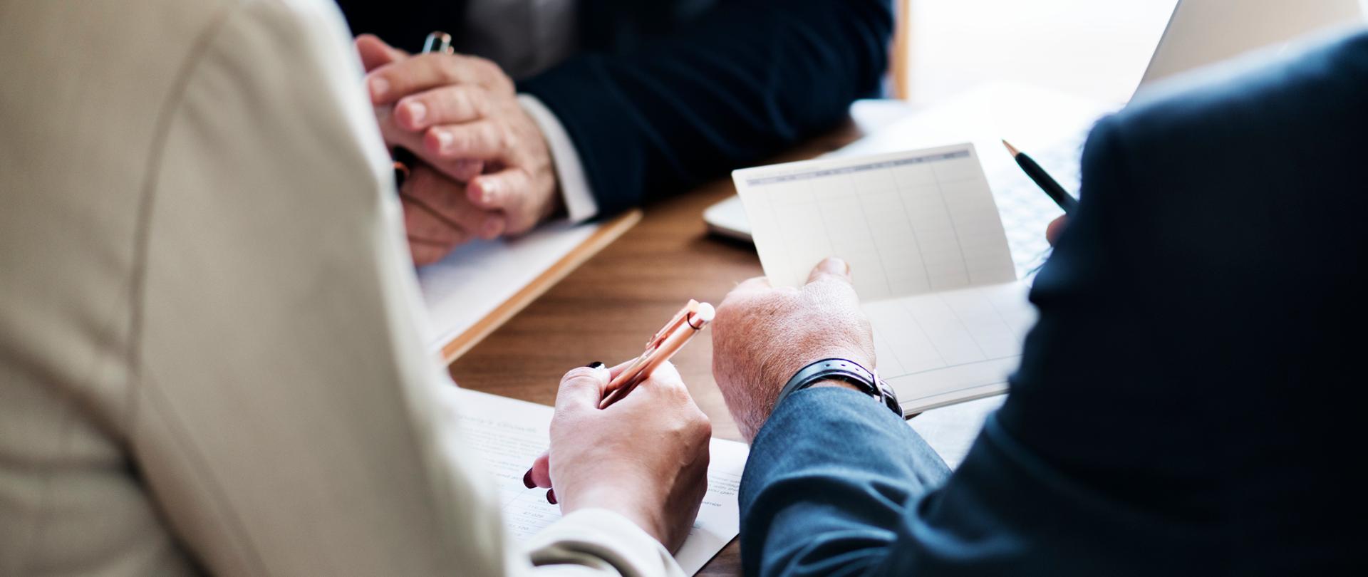 Dłonie trzech osób trzymające długopisy oraz dokumenty na biurku