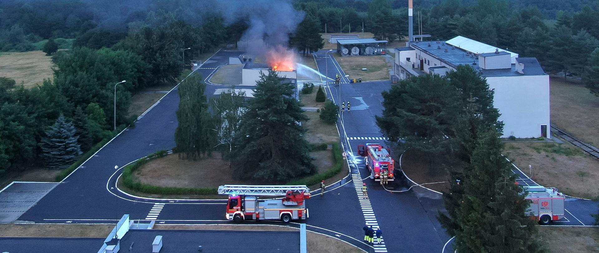 Zdjęcie przedstawia pojazdy pożarnicze i palący się zakład produkcyjny