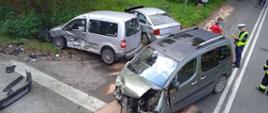Na zdjęciu widoczne rozbite samochody osobowe, policjant oraz uczestnik zdarzenia.