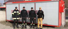 Zastępca Komendanta Centralnej Szkoły PSP w towarzystwie dwóch druhów OSP Zawiercie-Marciszów oraz oficera CS PSP na tle przekazywanego kontenera dekontaminacyjnego
