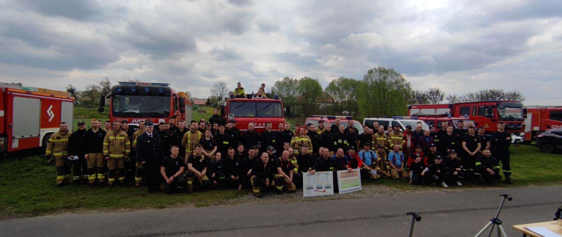 Zdjęcie zbiorowe wszystkich uczestników warsztatów szkoleniowych. W tle za strażakami widać samochody pożarnicze