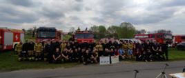 Zdjęcie zbiorowe wszystkich uczestników warsztatów szkoleniowych. W tle za strażakami widać samochody pożarnicze