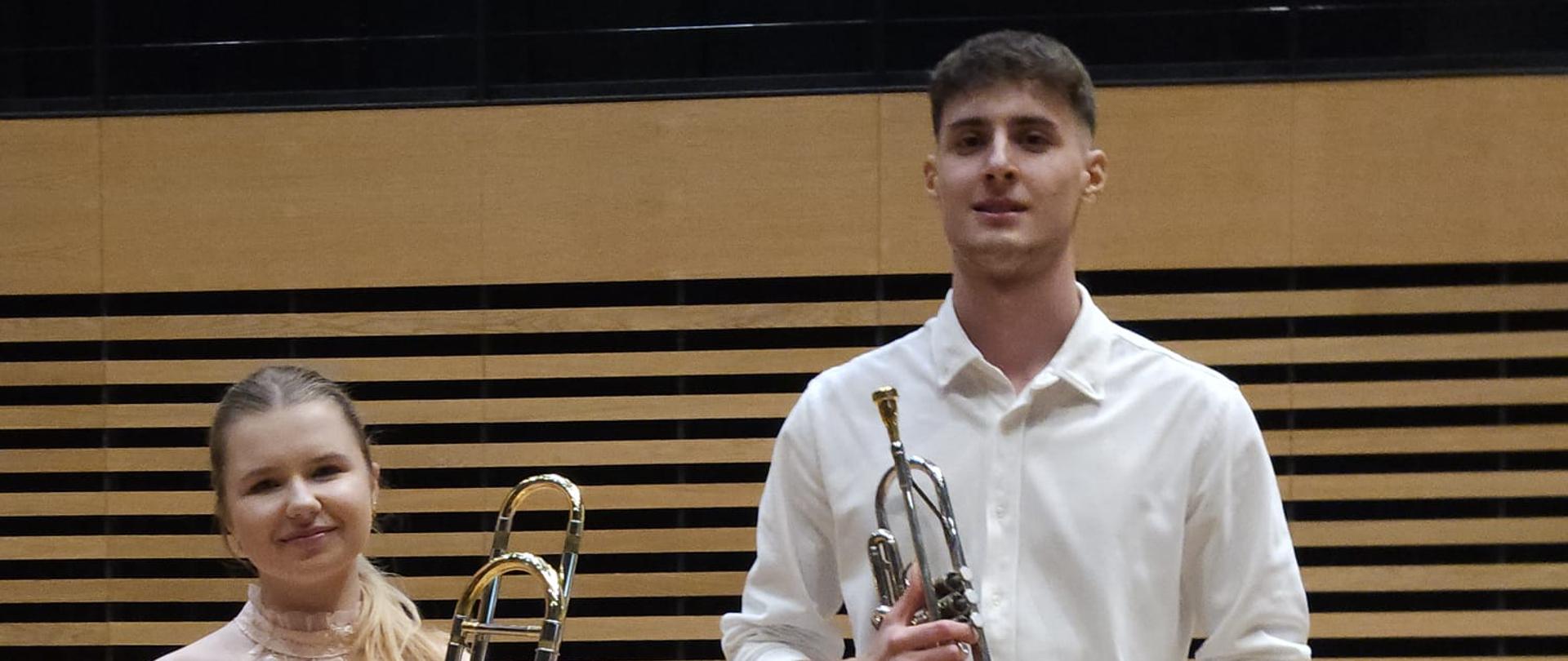 Dziewczyna i chłopak stoją na scenie z puzonem i trąbką.