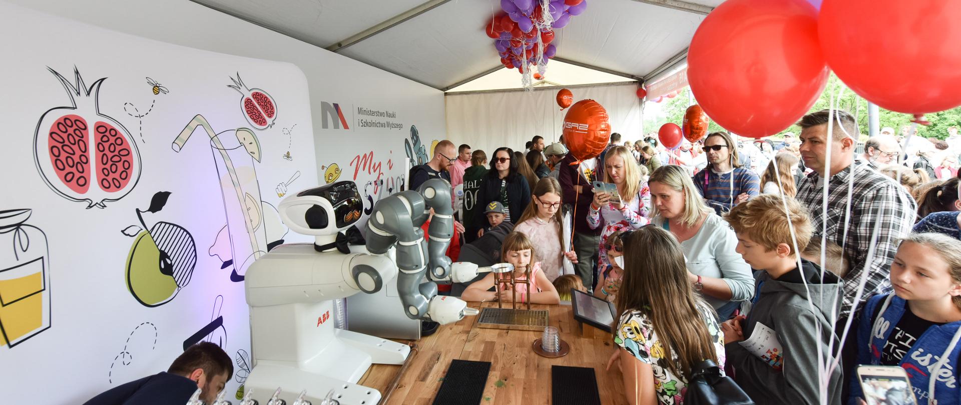 23. Piknik Naukowy - stoisko MNiSW. Po lewej stronie roboty, po prawej wielu zwiedzających, głównie dzieci.