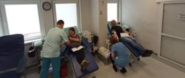 Na zdjęciu kobieta po lewej w szarej koszulce i czarnych spodniach po prawej mężczyzna w czarnej koszulce i dżinsach siedzą na granatowych fotelach oddają krew w pomieszczeniu o białych ścianach i szarej posadzce w Regionalnym Centrum Krwiodawstwa i Krwiolecznictwa w Oddziale Terenowym w Gorlicach.