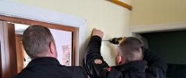 Strażacy za pomocą wiertarki wywiercają dziury w ścianie, które posłużą do montażu czujniki.