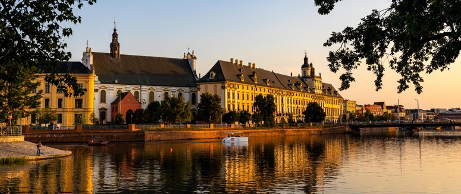 
Widok na budynki starego miasta z Uniwersytetem Wrocławskim i nabrzeżem ulicy o zachodzie słońca nad rzeką (Wrocław, Polska)