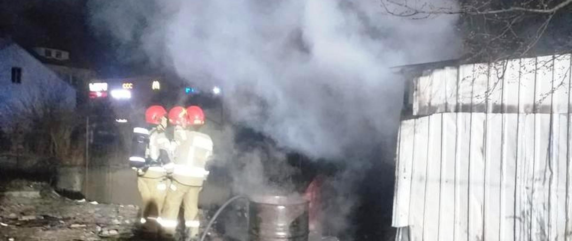 Dym wydobywający się z garażu blaszanego a obok strażacy.