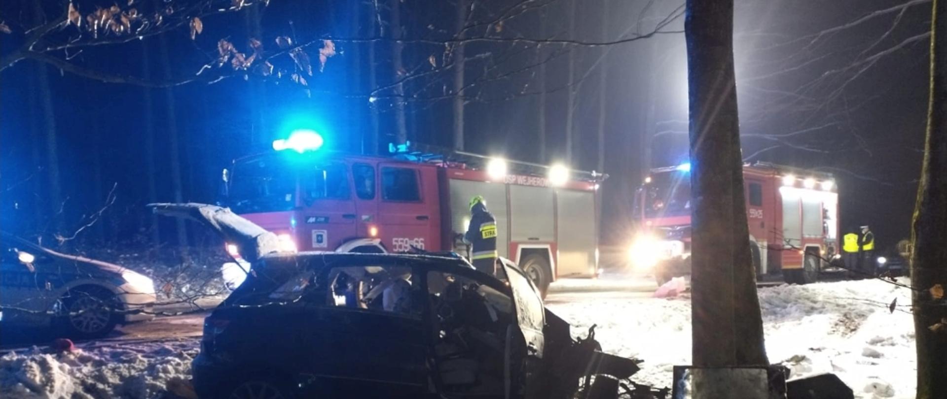 na zdjęciu widoczne jest miejsce wypadku drogowego, pojazd osobowy który uderzył w drzewa i wozy straży pożarnej