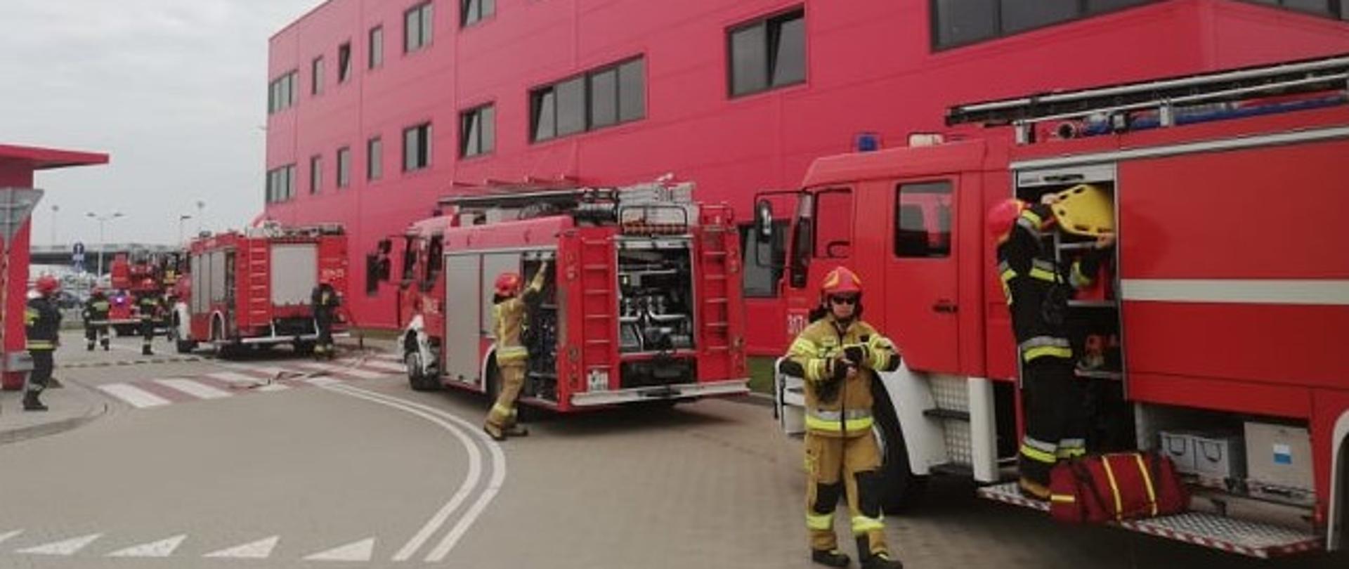 Na zdjęciu widoczny jest budynek terminala, trzy samochody straży pożarnej oraz pracujący strażacy.