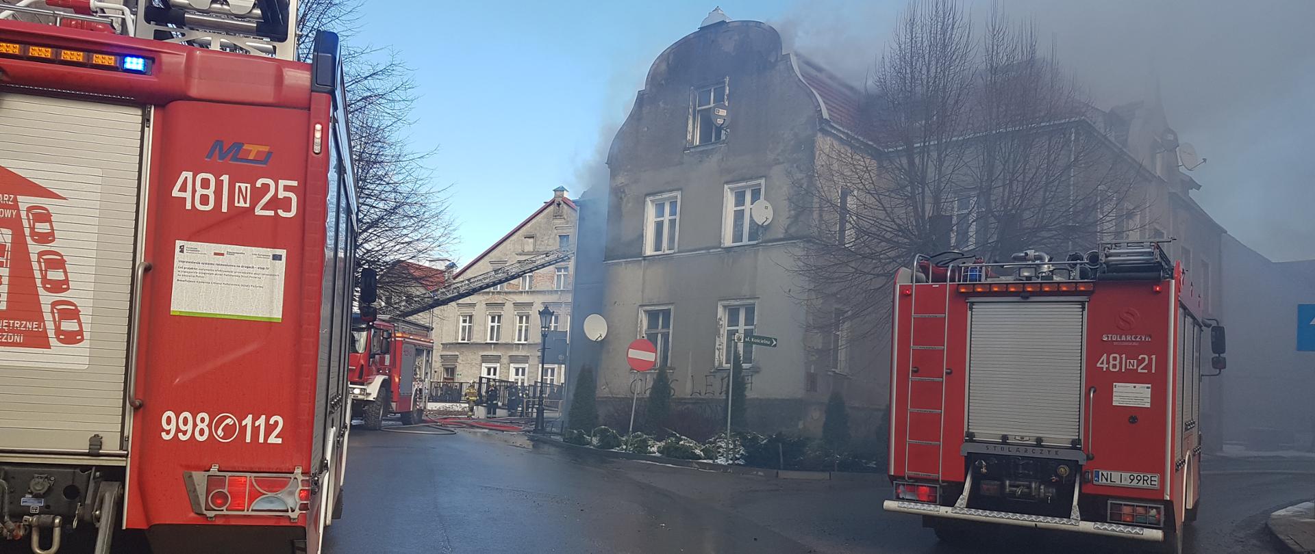 Zdjęcie przedstawia trzy pojazdy pożarnicze ustawiona obok palącej się kamienicy