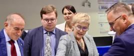 Wiceminister Mrówczyńska i trzech mężczyzn w garniturach stoją i rozmawiają nad otwartym laptopem.
