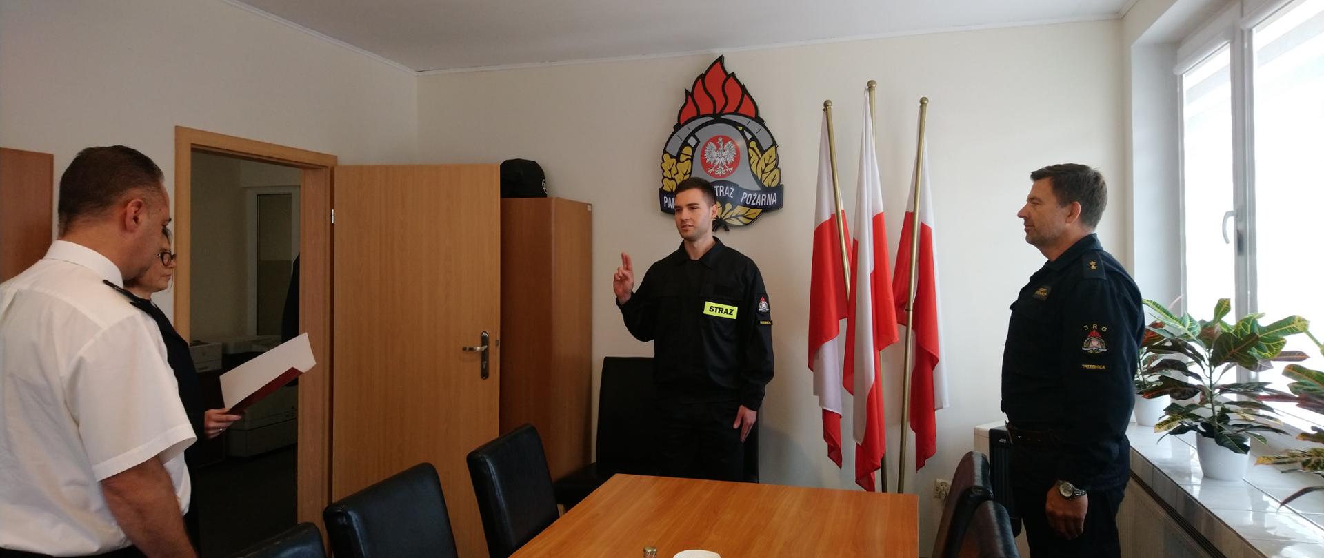 Strażak w mundurze służbowym czarnym składający ślubowanie przed Komendantem Powiatowym i Dowódcą Jednostki.
