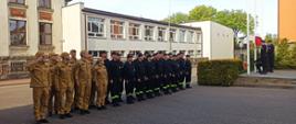 Pododdział funkcjonariuszy Państwowej Straży Pożarnej oddaje honor podczas podnoszenia flagi państwowej na maszt.