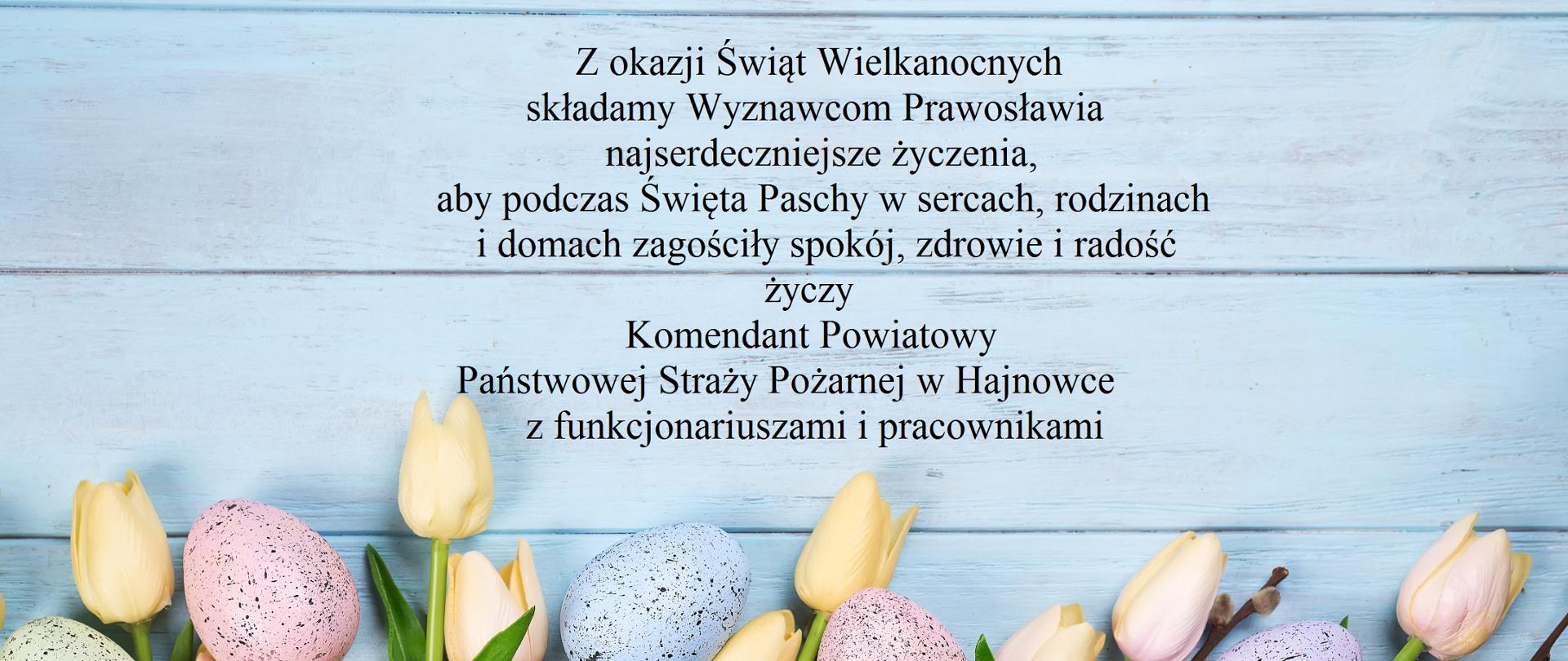 Na niebieskim tle u dołu z jajkami i kwiatami życzenia Komendanta Powiatowego w Hajnówce