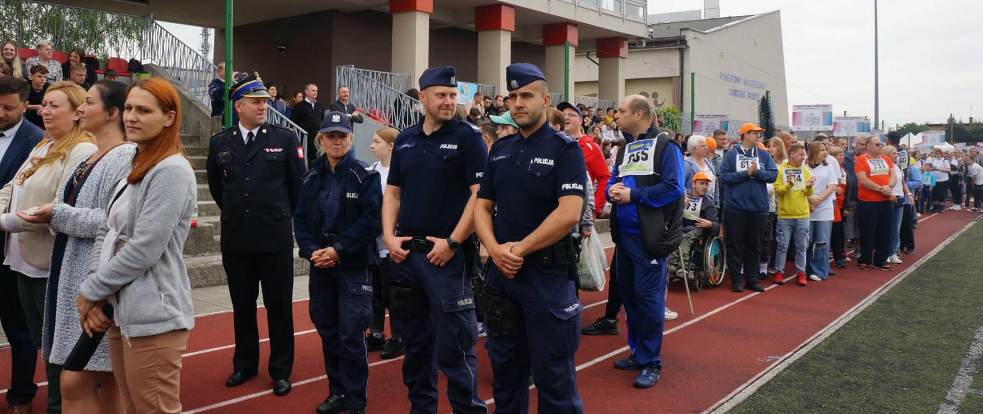 Na zdjęciu policjanci, strażak oraz zawodnicy na płycie boiska startujący w olimpiadzie
