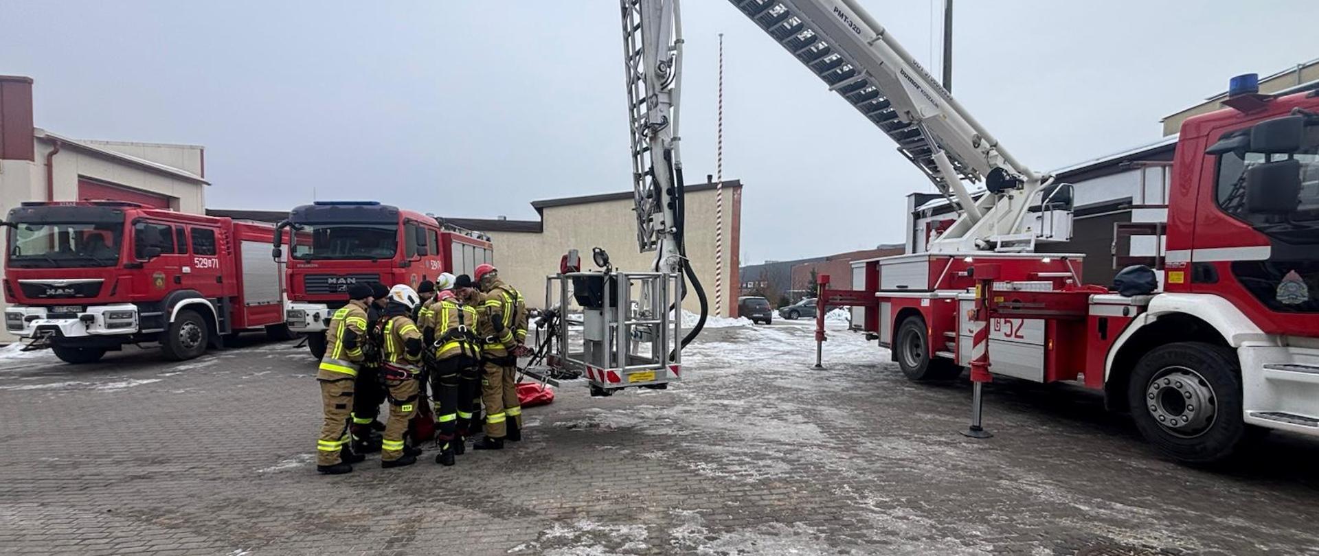 Na zdjęciu grupa strażaków OSP podczas szkolenia, w tle budynki PSP i samochody pożarnicze