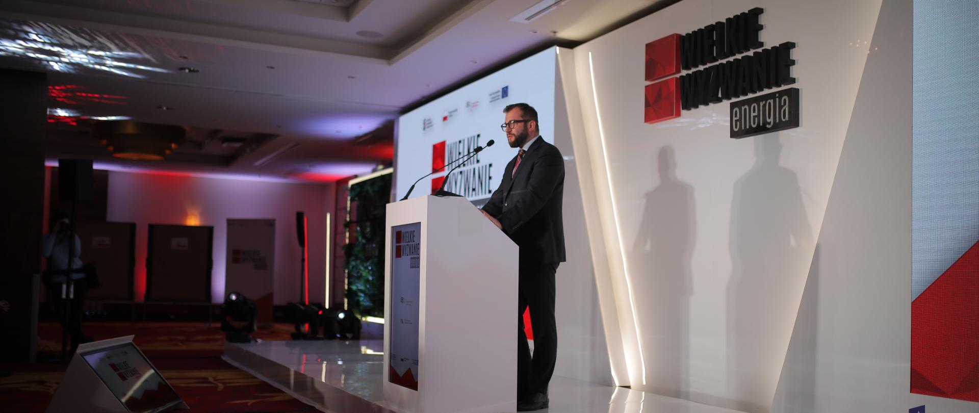Minister Grzegorz Puda stoi przy mównicy. Za nim wyświetlony jest napis "Wielkie wyzwanie:energia". 