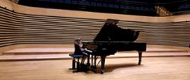 Dziewczynka gra na fortepianie Fazioli na estradzie sali koncertowej.