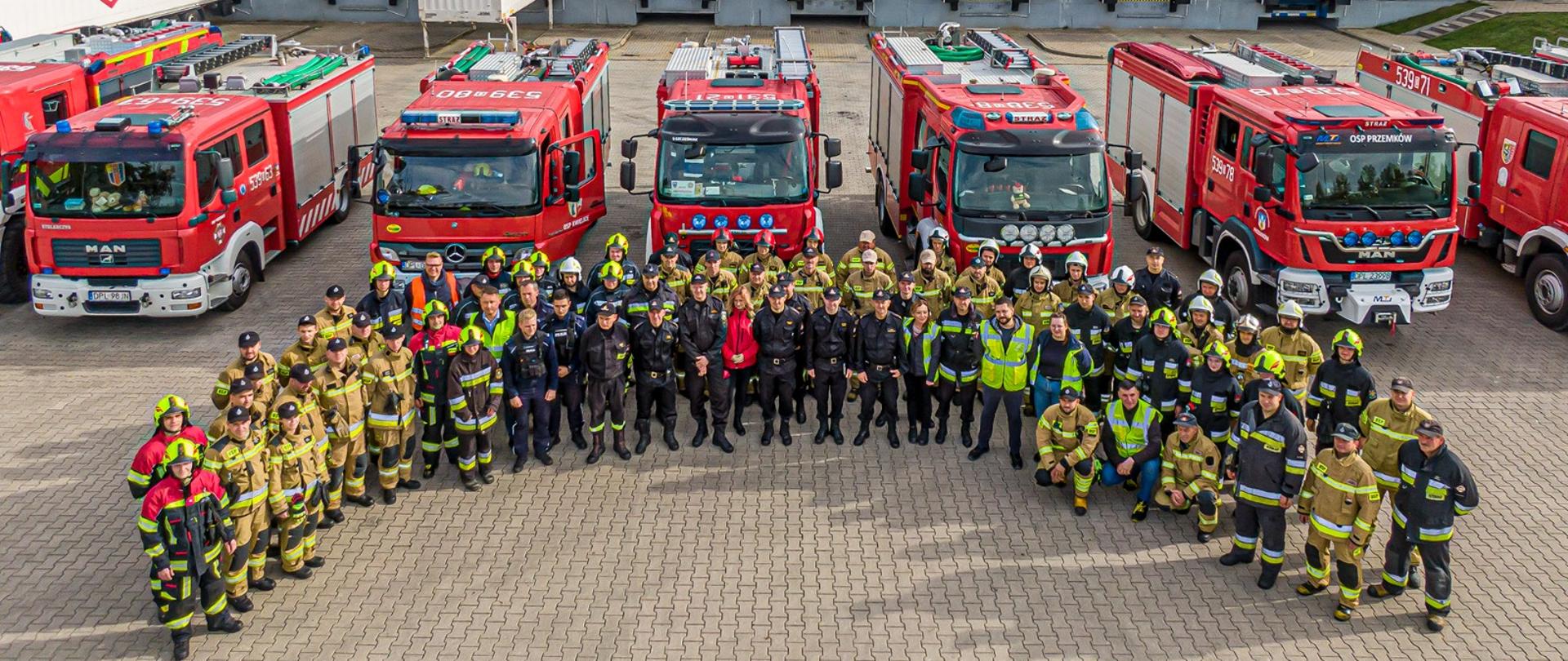 Zdjęcie grupowe ratowników JOP na tle aut pożarniczych