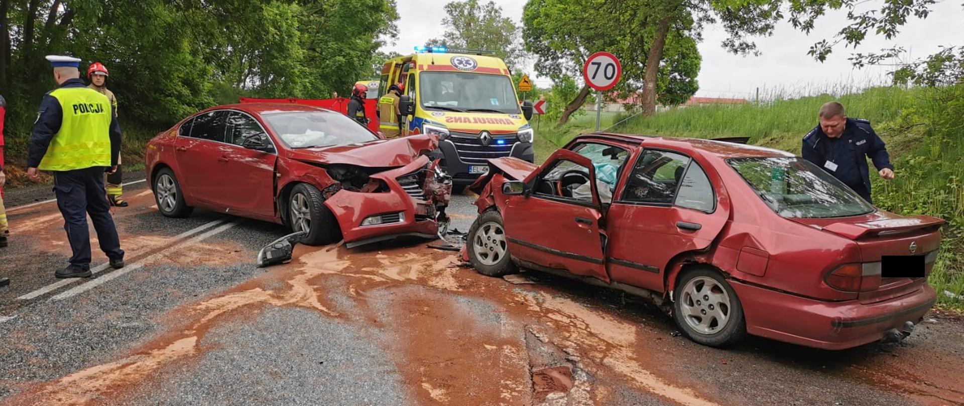 Dwa samochodu koloru bordowego po wypadku czołowym na skrzyżowaniu w miejscowości Rogów Wieś. Uszkodzone przodu obu pojazdów oraz plama płynów eksploatacyjnych posypana sorbentem