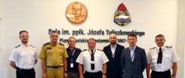 W szeregu ustawieni członkowie SITP wraz z Komendantem Wojewódzkim PSP woj. pomorskiego. W tle ściana z napisem "Sala imienia podpółkownika Józefa Tuliszkowskiego - pioniera polskiego pożarnictwa.