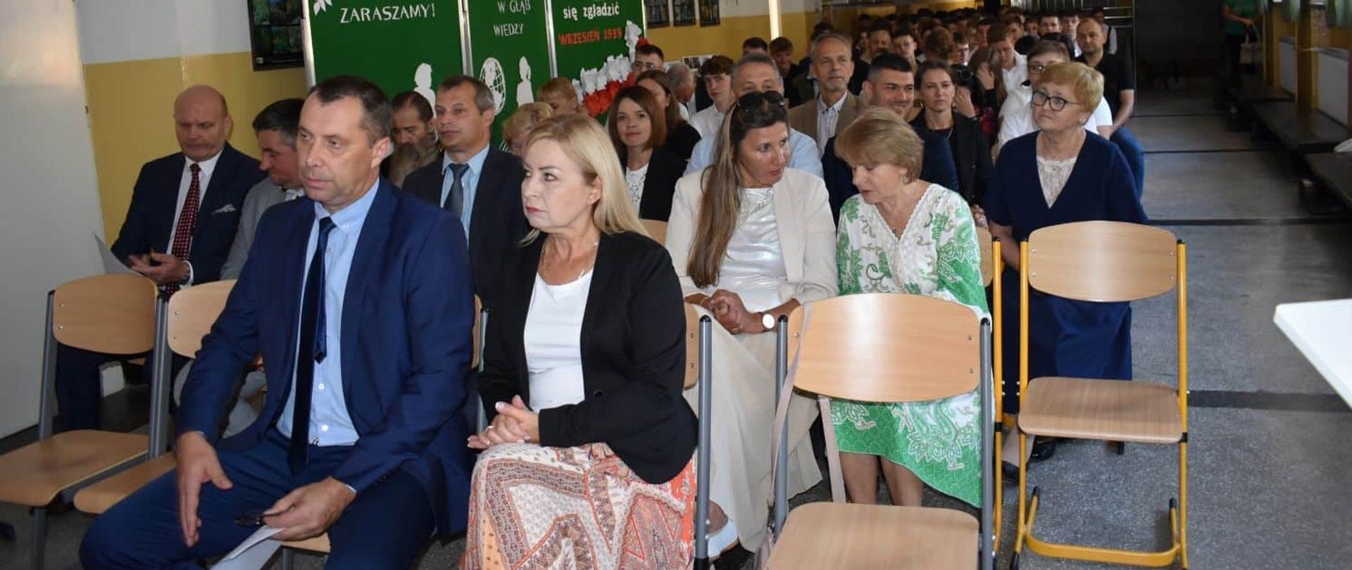 Widok na zaproszonych gości siedzących w pierwszych rzędach podczas uroczystości. W tle widać dekoracje ścienne dotyczące rocznicy września 1939 roku.