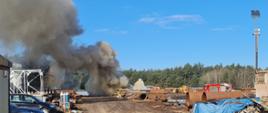 Na zdjęciu widać teren zakładu, na którym doszło do pożaru. W oddali widać strażaków gaszących pożar otuliny rur w postaci pianki poliuretanowej.