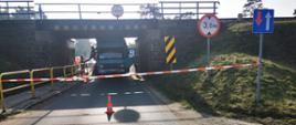 Na zdjęciu widać zaklinowany pojazd ciężarowy pod wiaduktem kolejowym, po prawej stronie widać znak informujący o przejeździe o wysokości 3 m. Droga jest zablokowana przez zaklinowany pojazd. 