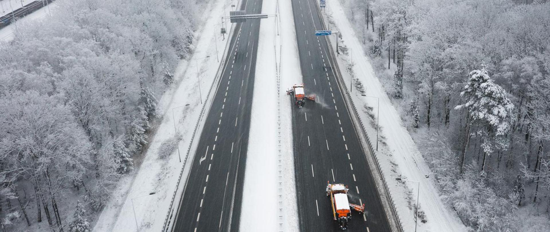 pługi odśnieżają drogę szybkiego ruchu biegnącą przez zaśnieżony las, zdjęcie lotnicze