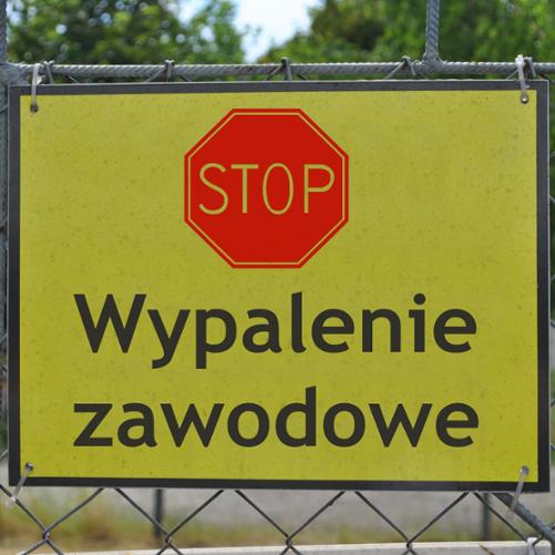Na ogrodzeniu wisi żółta tablica, na której znajduje się czerwony znak „STOP" a pod nim czarny napis „Wypalenie zawodowe".