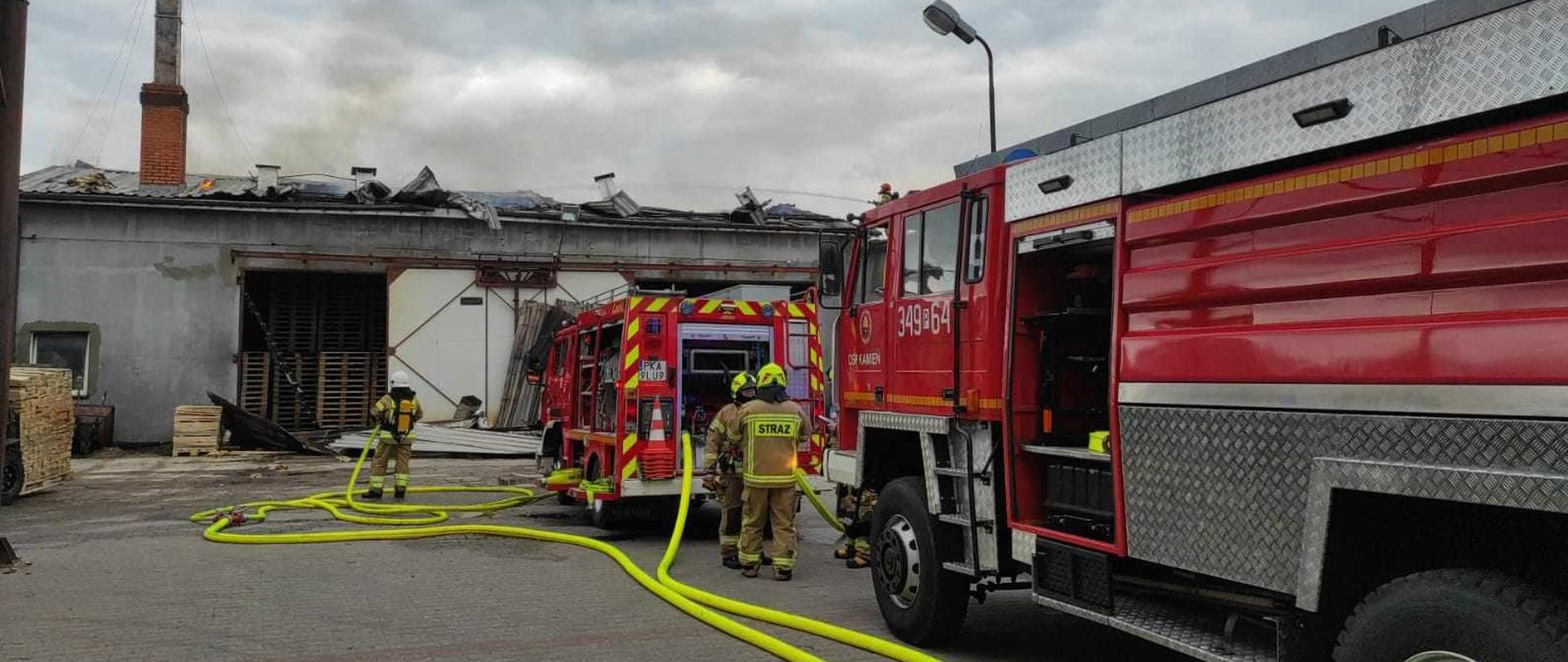 Samochody strażackie do których podłączone są węże. 