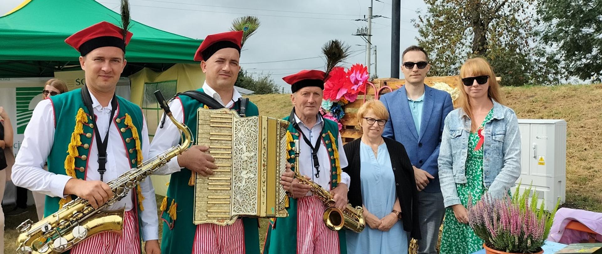 Inspektorzy na wspólnej fotografii z kapelą ludowa przy stoisku promocyjnym.