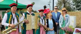 Inspektorzy na wspólnej fotografii z kapelą ludowa przy stoisku promocyjnym.