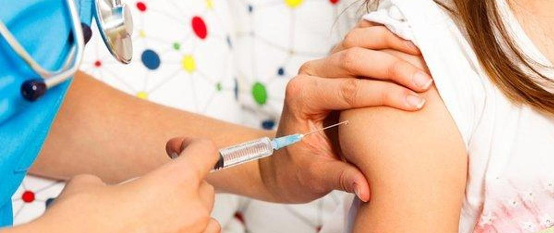 pielęgniarka w niebieskim fartuchu i stetoskopem wykonuje zastrzyk w odsłonięte ramię dziewczynki