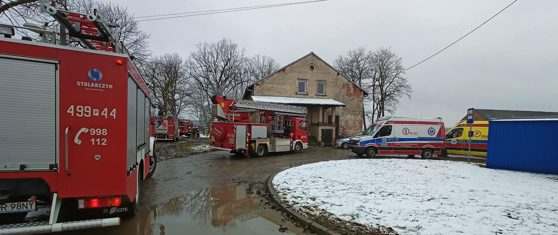 Zdjęcie przedstawia samochody służb ratowniczych (Straży Pożarnej, Zespołów Ratownictwa Medycznego i Policji), pojazdy stoją przy budynku, w którym doszło do pożaru. 