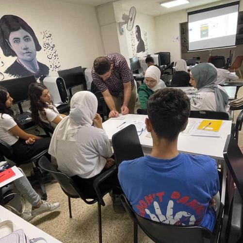 W pracowni komputerowej siedzi kilkanaście młodych kobiet i mężczyzn, jeden mężczyzna coś pokazuje zaś reszta go obserwuje