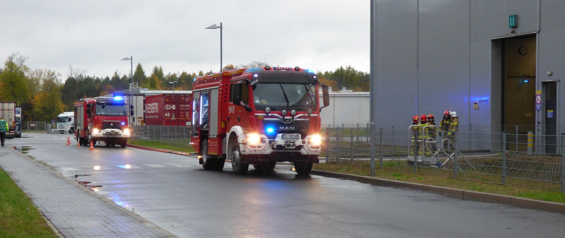 dwa wozy strażackie stoją przez zakładem 