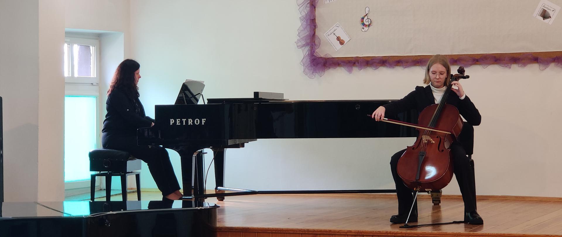 Zdjęcie przestawiające Magdalenę Świderską na wiolonczeli z akompaniamentem fortepianowym Doroty Straburzyńskiej podczas koncertu w auli szkoły.