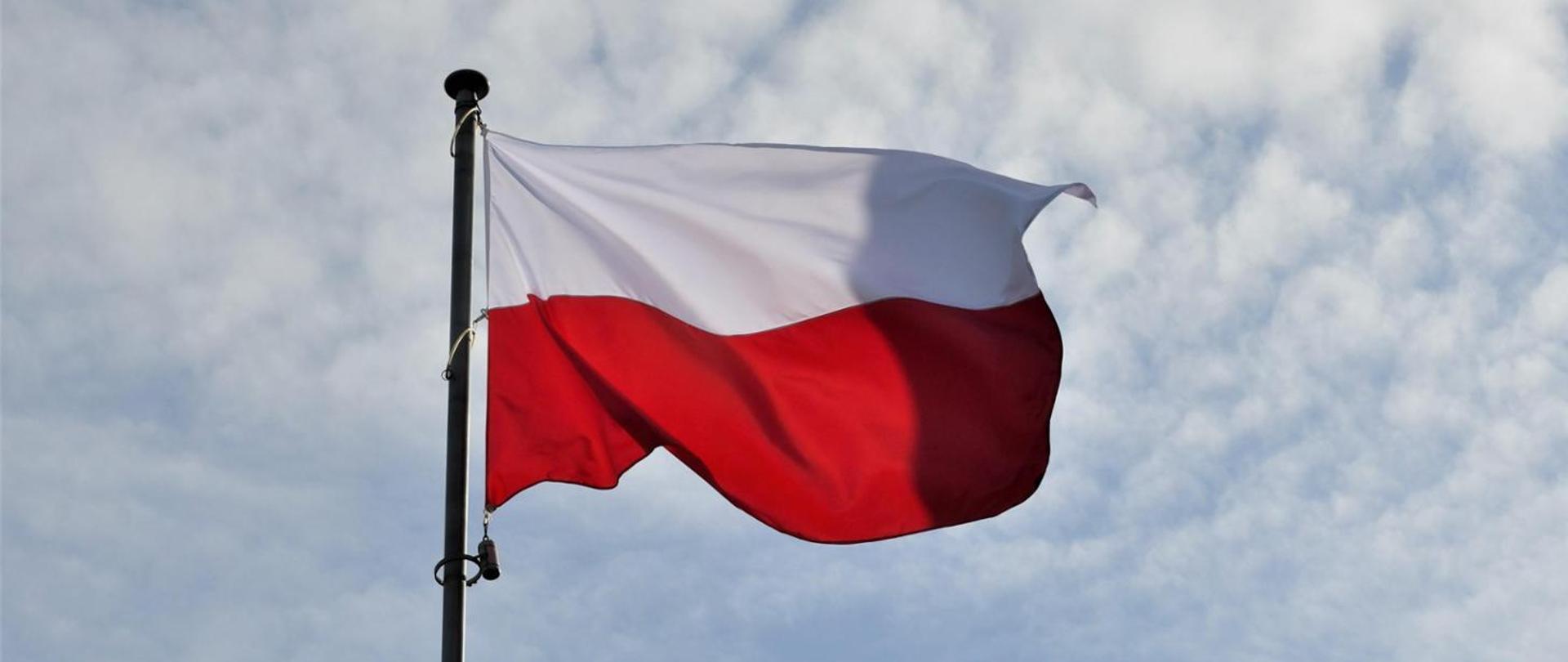 
Polska flaga powiewa na tle pochmurnego nieba.