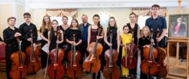 Zdjęcie grupowe osób w sali muzycznej, wszyscy trzymają wiolonczelę
