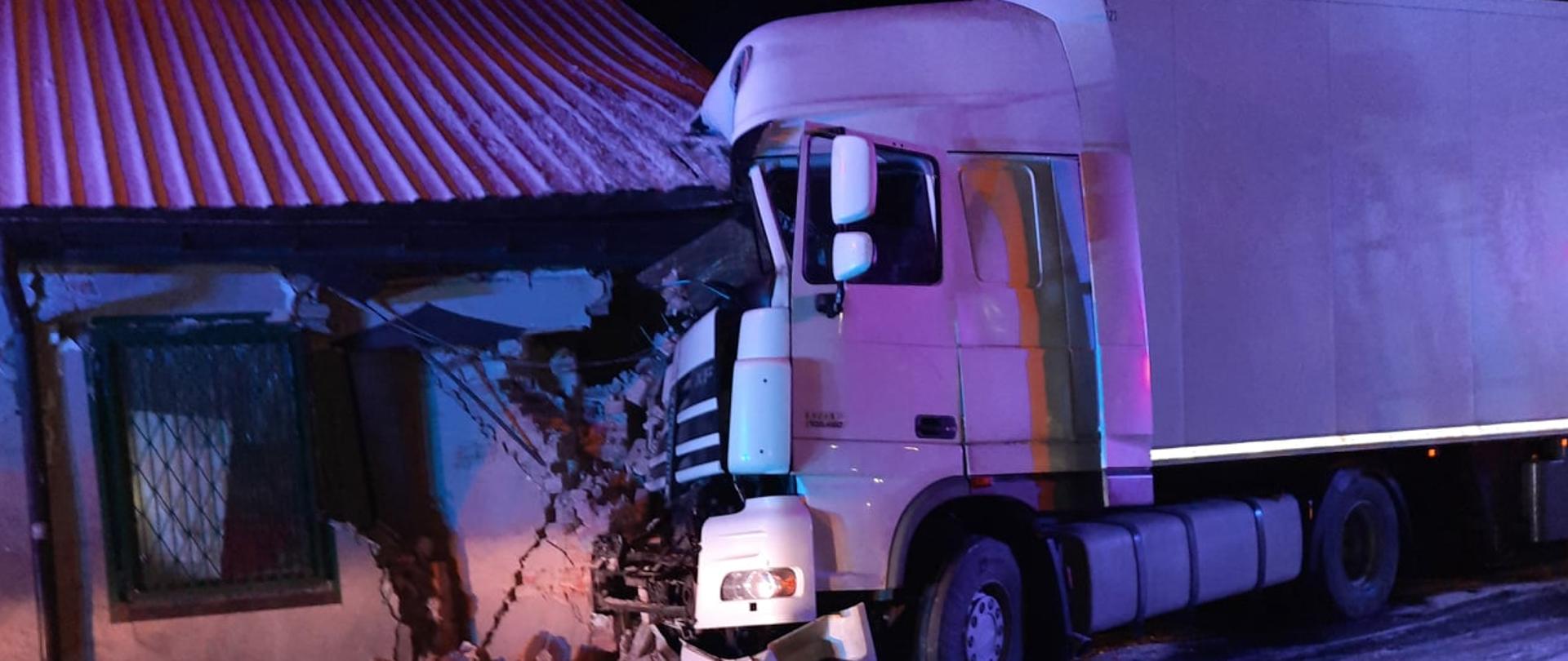 Zdjęcie zrobione w nocy przedstawia białego tira, który wjechał w nieużywany parterowy budynek usługowy.