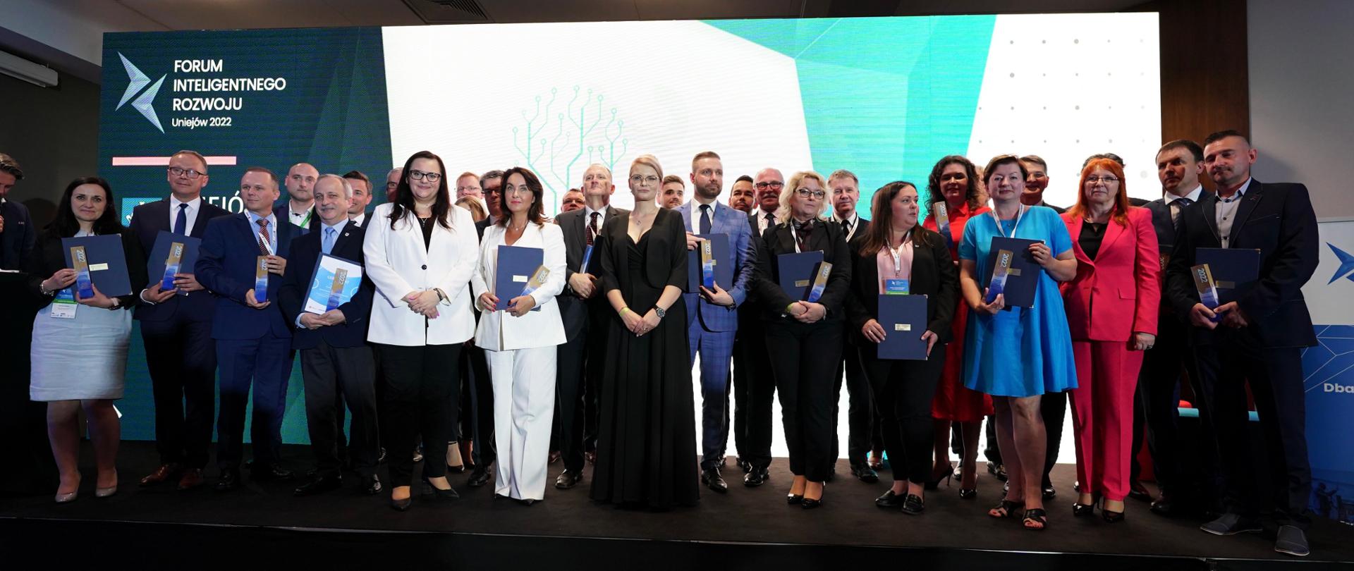 Grupa osób na scenie ze statuetkami i dyplomami