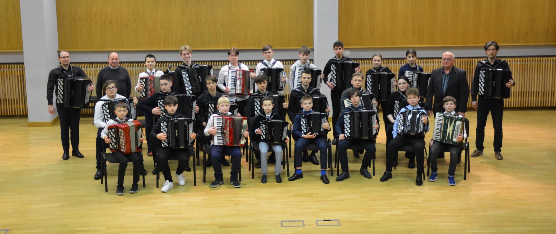 Uczniowie i pedagodzy orkiestry trzymający akordeony ustawieni w trzech rzędach.