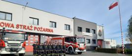 Na zdjęciu strażacy śpiewają hymn na tle budynku komendy straży pożarnej