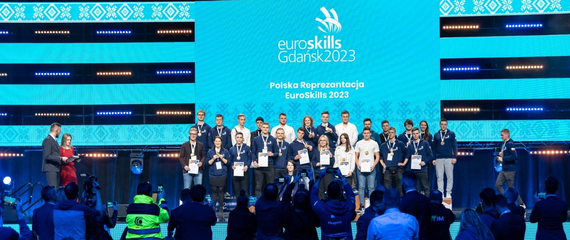 Zdjęcie sceny na której są nagrodzeni medalami i dyplomami.