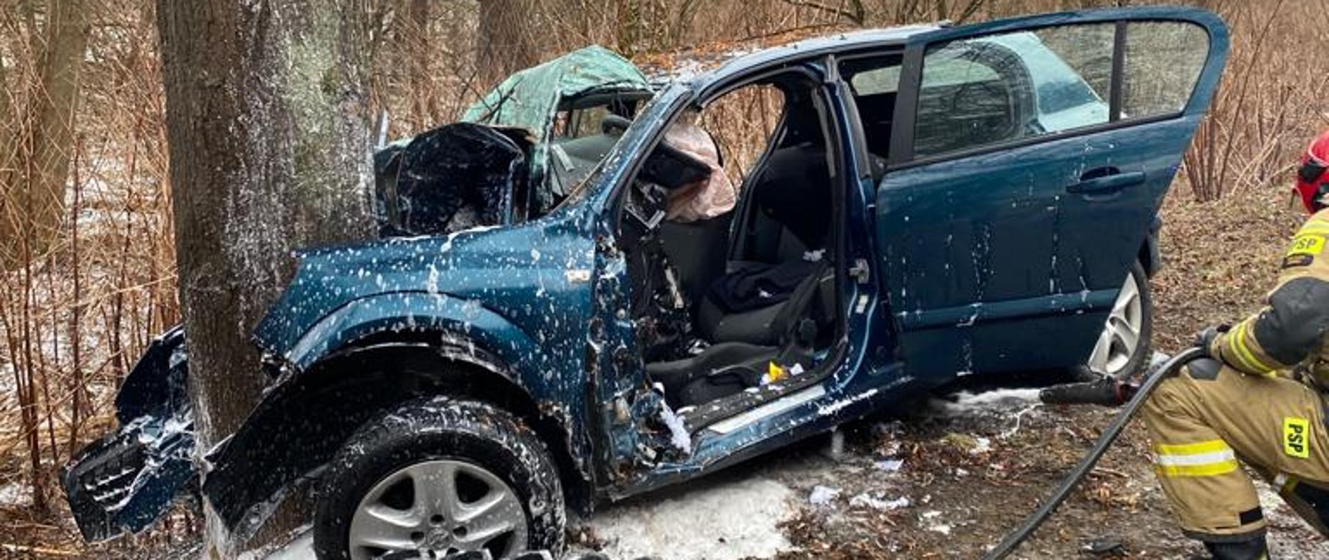 Samochód osobowy, który uderzył w drzewo i strażak z linią wężową